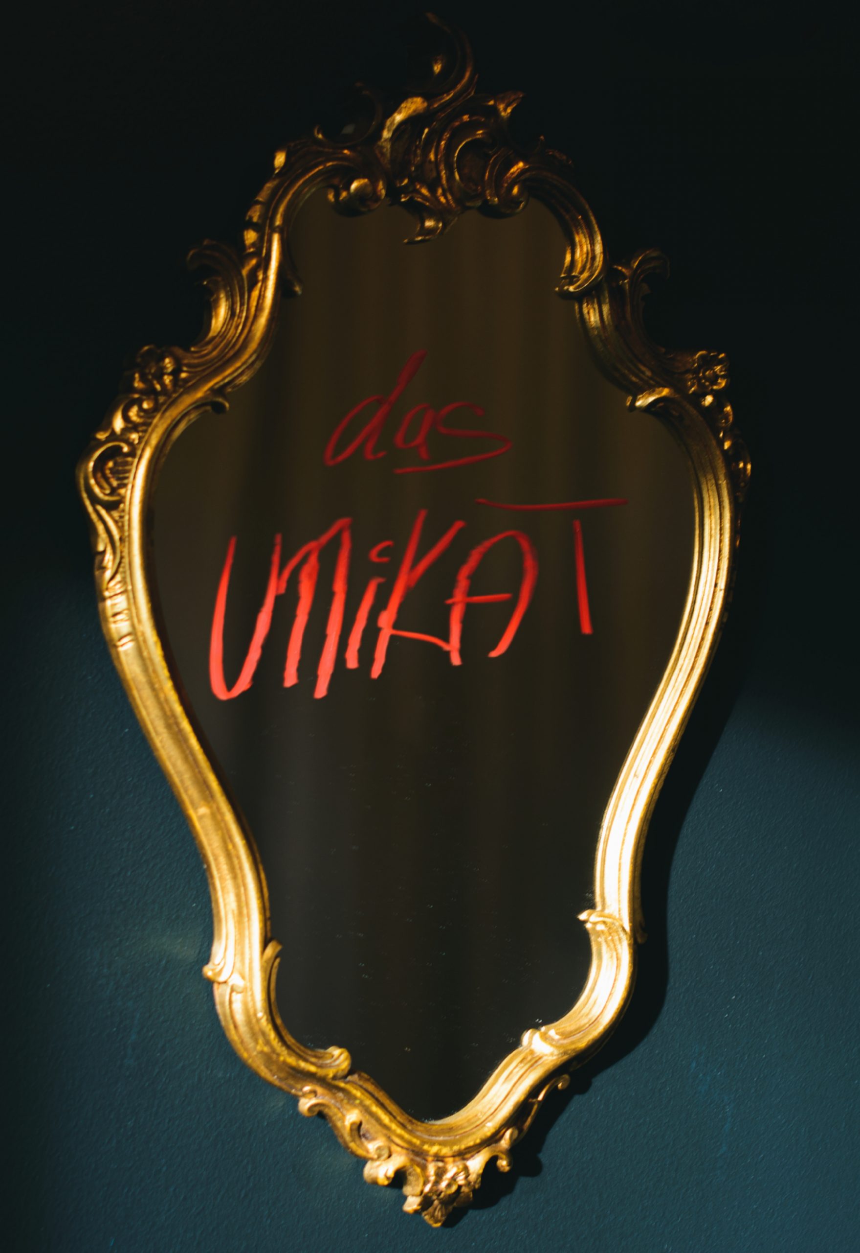Verschnörkelter Vintage-Spiegel mit dem Schriftzug „das UNiKAT“ in Rot auf dem Glas.